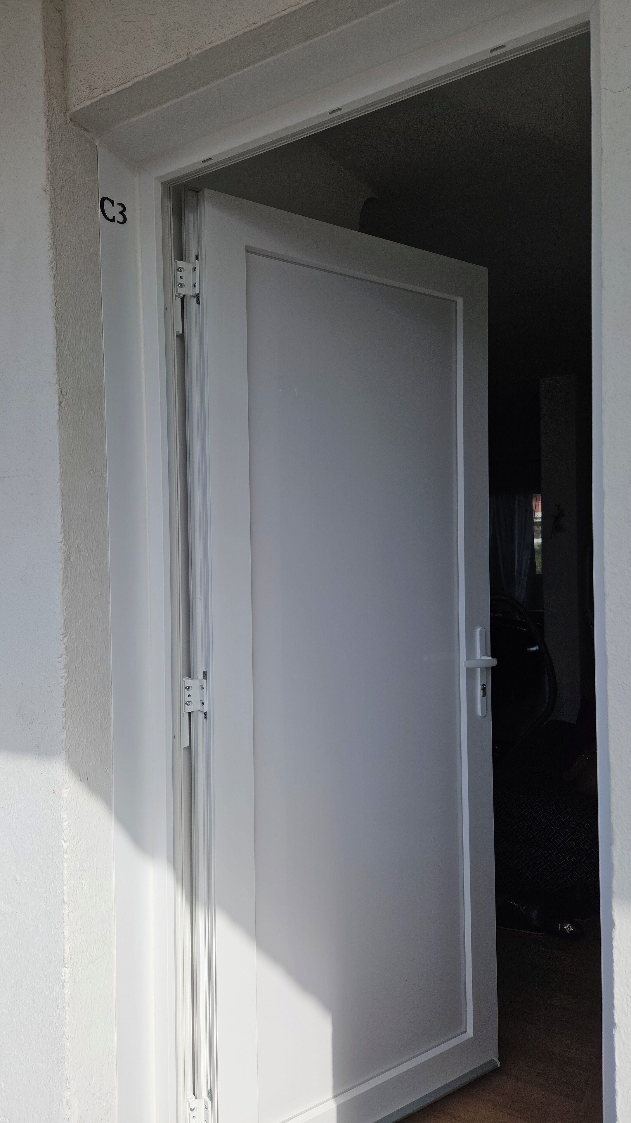 Een witte deur met een hendel, een zichtbaar ‘C3’ label, en een schaduw op de muur.