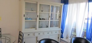 Une pièce avec un meuble blanc aux portes en verre, une table en verre et deux chaises noires.