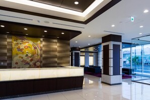 Eine moderne Hotelhalle mit einer Rezeption, einer großen Wanddekoration und einer Glastrennwand.