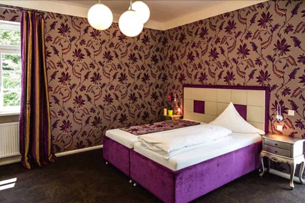 A room with a bed, a nightstand, a lamp, and a window with curtains.