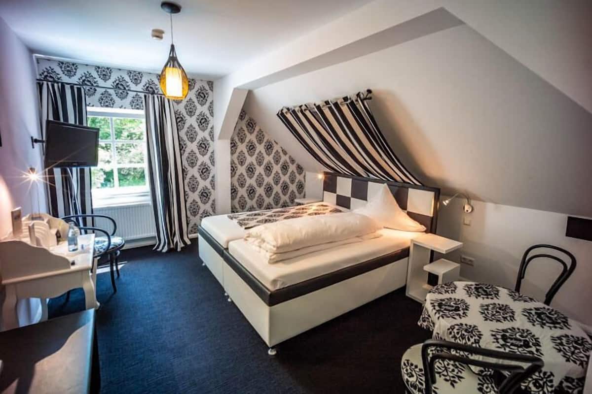 A bedroom with a bed, a desk, a chair, a TV, and a window with curtains.
