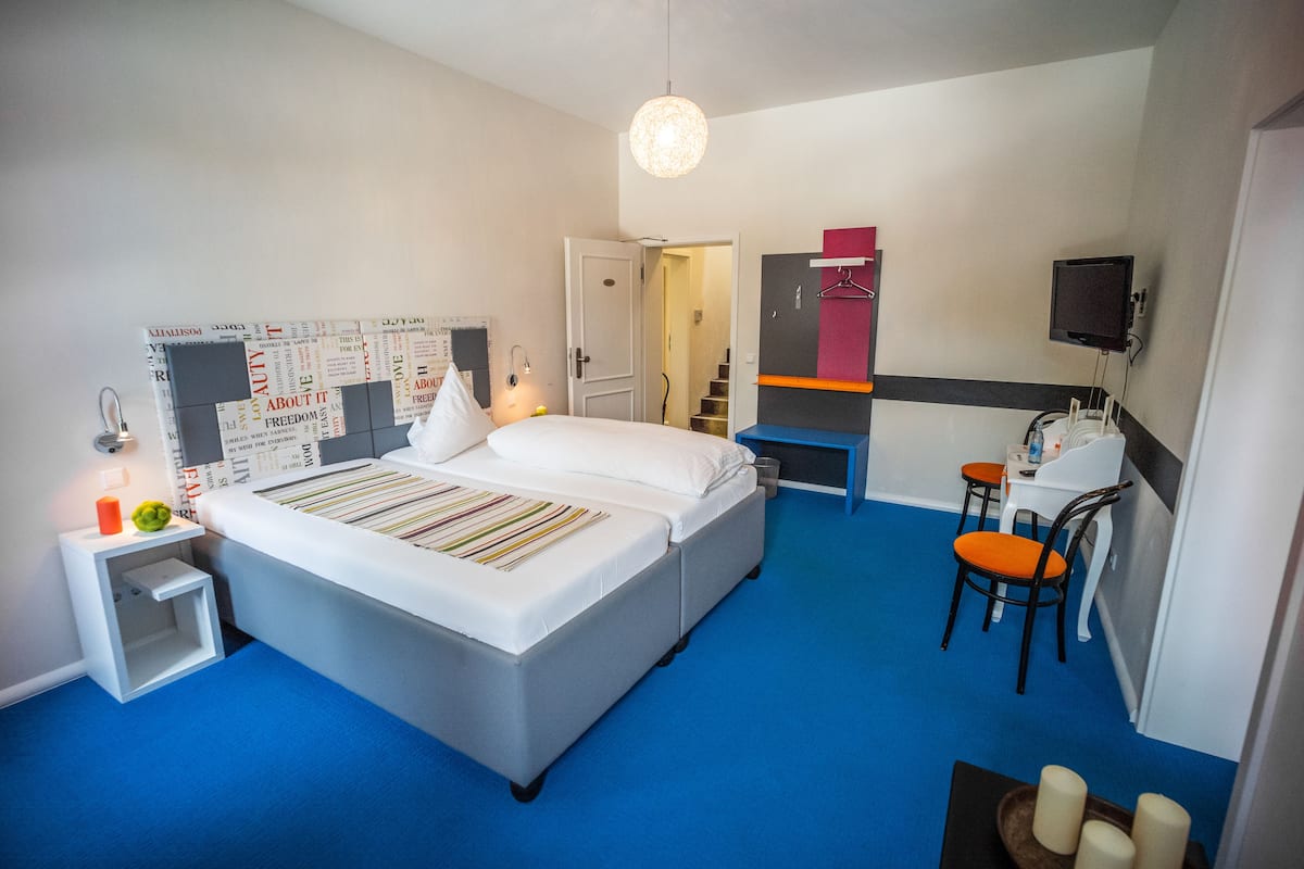 A modern hotel room with a large bed, a desk with a chair, a television, and a small seating area.