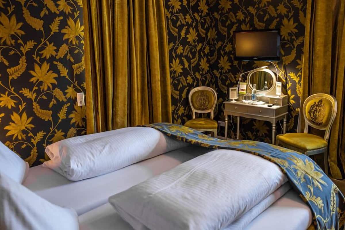 A hotel room with a bed, a vanity with a mirror, and a television on the wall.