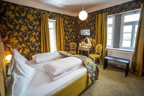 A hotel room with a bed, a desk, a chair, a television, and a window with curtains.