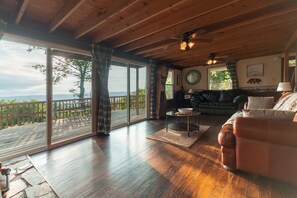 A spacious living room with a wooden ceiling, a large sliding glass door leading to a deck, a comfortable sofa, and a fireplace. - Clouds Mountain Cabin (Rileyville)