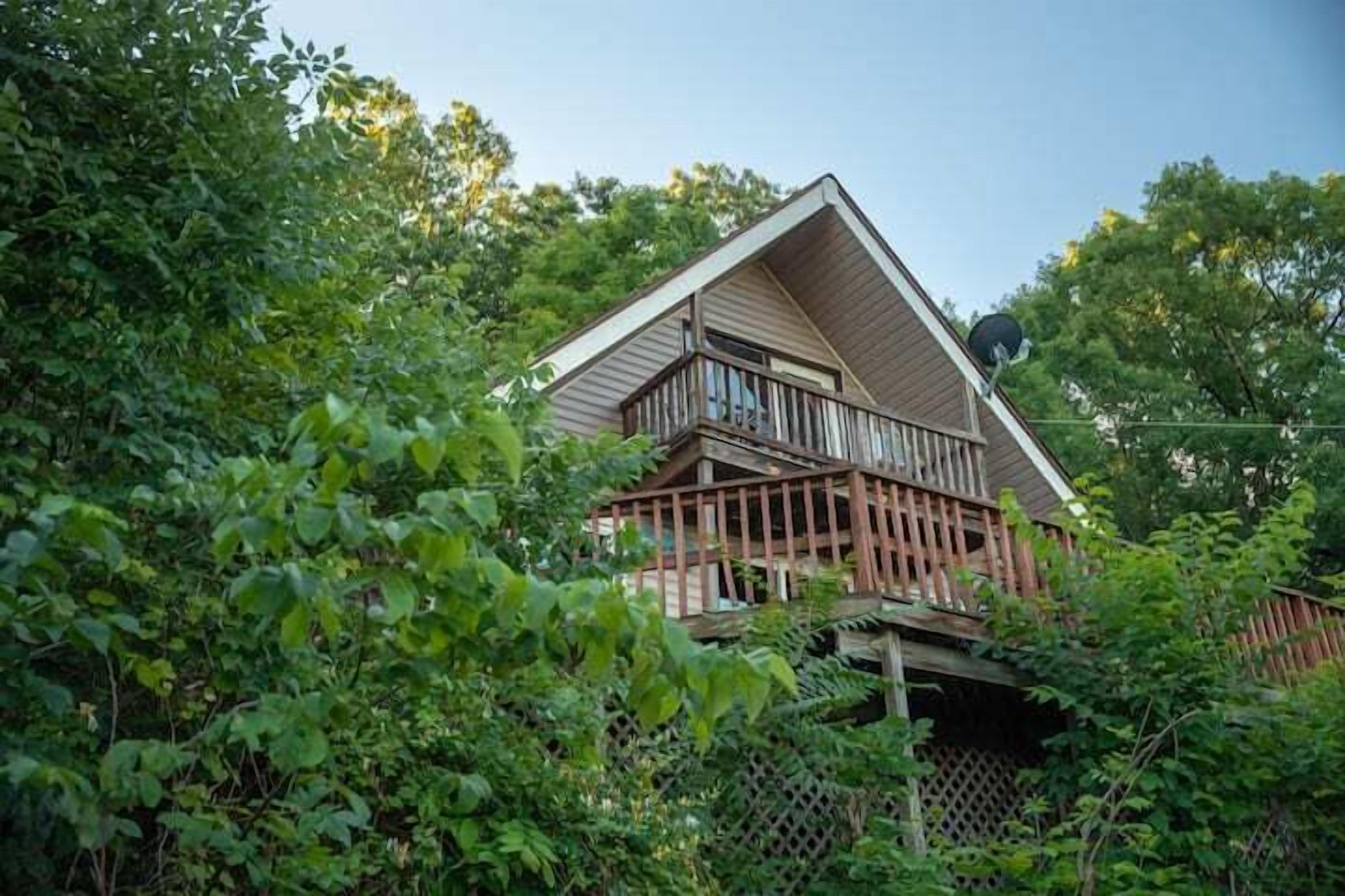 Een huis met een houten terras en een omheinde tuin, omgeven door weelderige begroeiing.