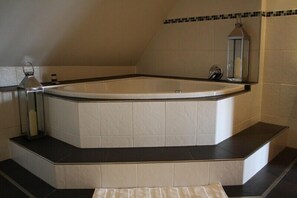 Une baignoire d’angle, entourée de carreaux noirs et blancs, un petit miroir et une serviette sur le sol.
