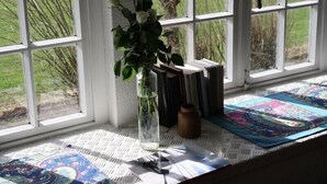 Una ventana con vistas a un campo cubierto de hierba, un florero con flores y una alfombra estampada en el alféizar.