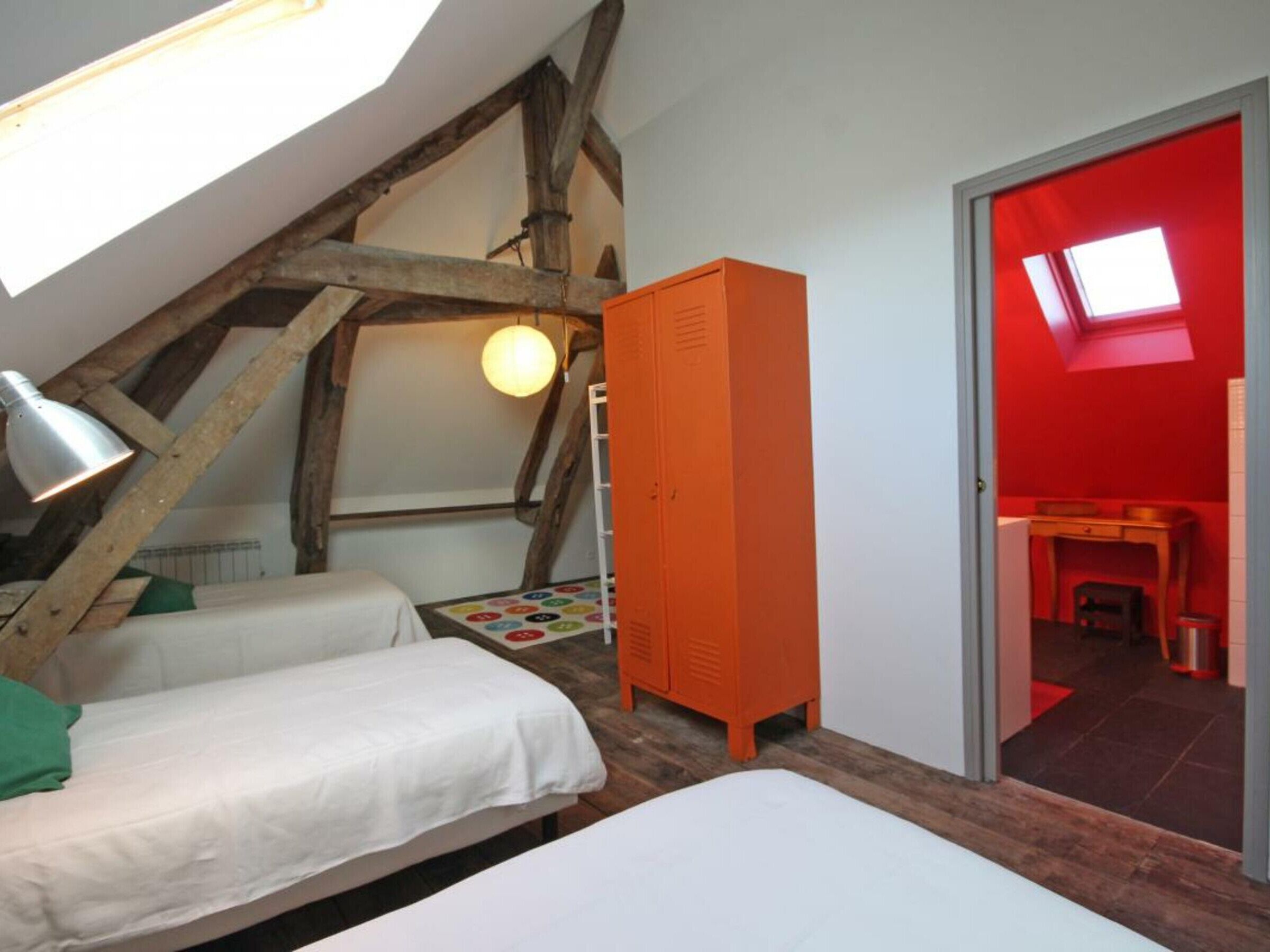 Un dormitorio con dos camas, techo de madera, armario naranja y tragaluz.