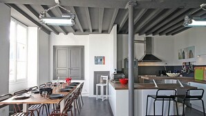 A modern kitchen with a central island, a dining area with a long table and chairs, and a large window providing natural light. - Spacious House with Indoor Pool and Wifi in Laleu (Laleu)