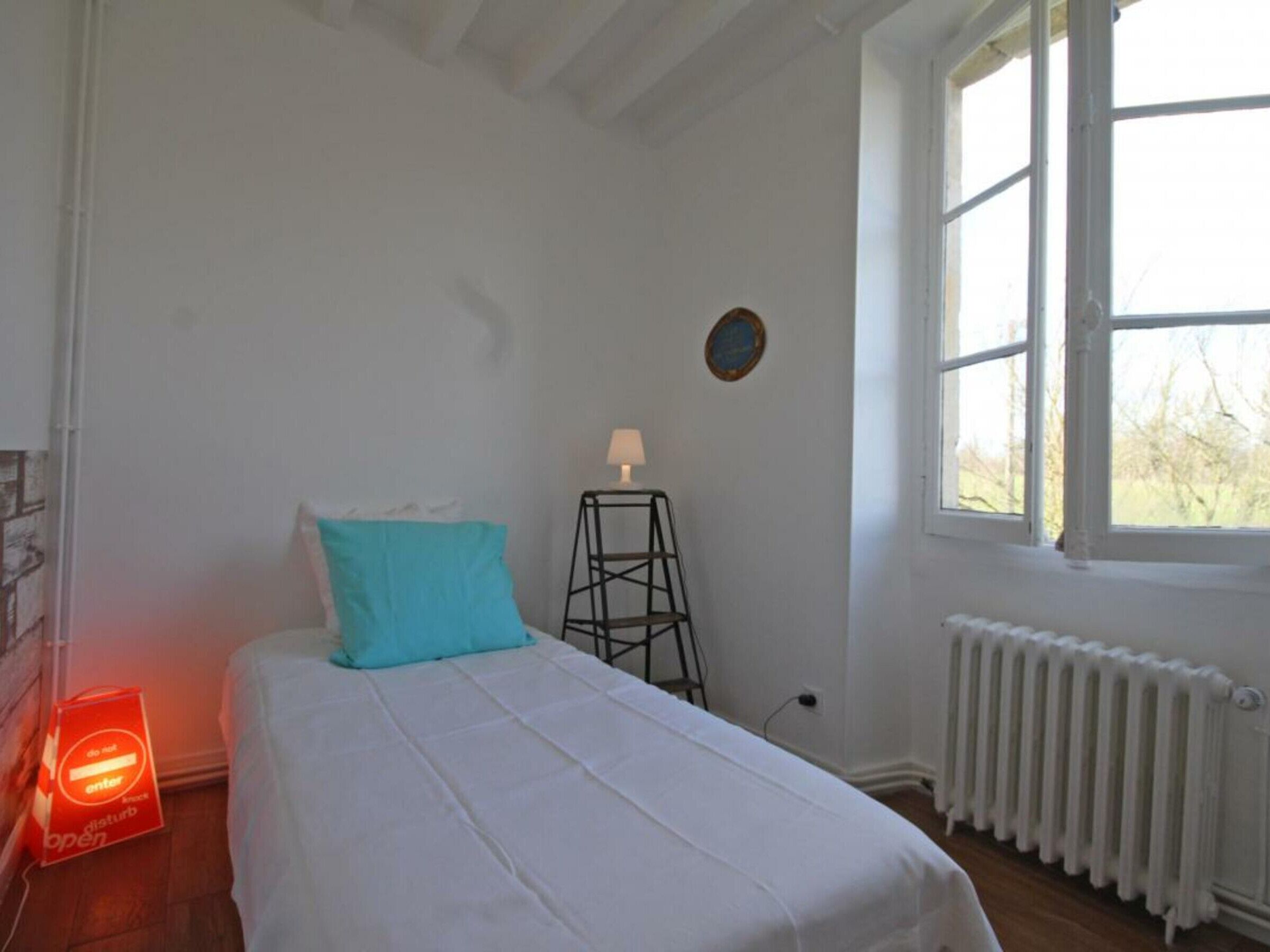 Ein Schlafzimmer mit Bett, Fenster, Heizkörper und einer Tür mit einem Schild.