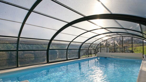 An indoor swimming pool with a curved roof structure, clear glass walls, and a view of the surrounding landscape. - Spacious House with Indoor Pool and Wifi in Laleu (Laleu)