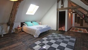 A bedroom with a checkered floor, a bed with a white bedspread and teal pillows, a small wooden stool, and a hanging light fixture. - Spacious House with Indoor Pool and Wifi in Laleu (Laleu)