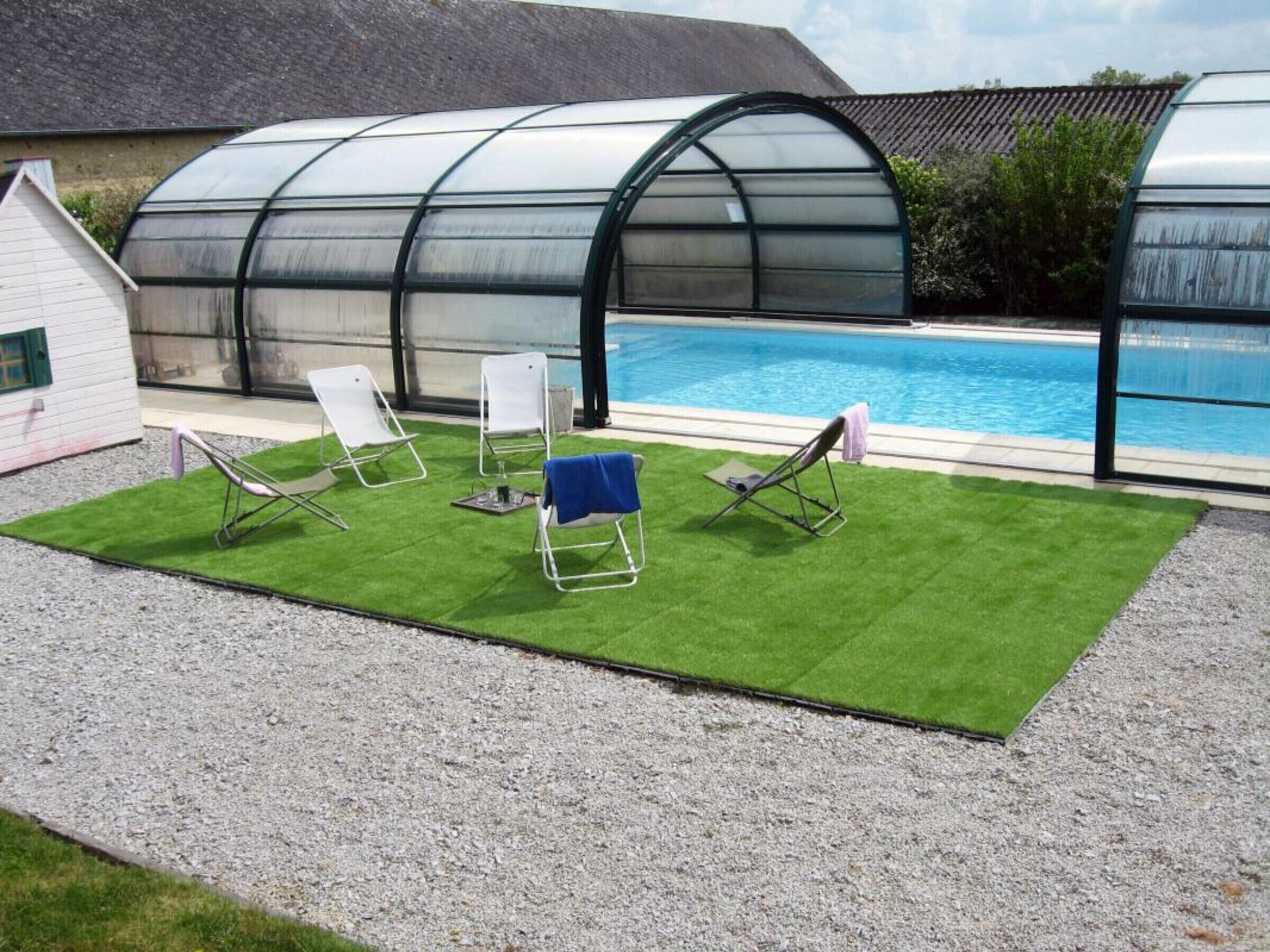 A pool area with a transparent greenhouse structure, artificial grass, and two lounge chairs.