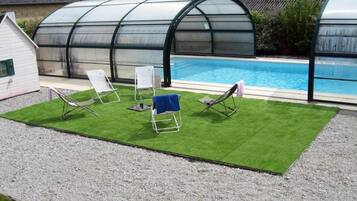 A pool area with a transparent greenhouse structure, artificial grass, and two lounge chairs.
