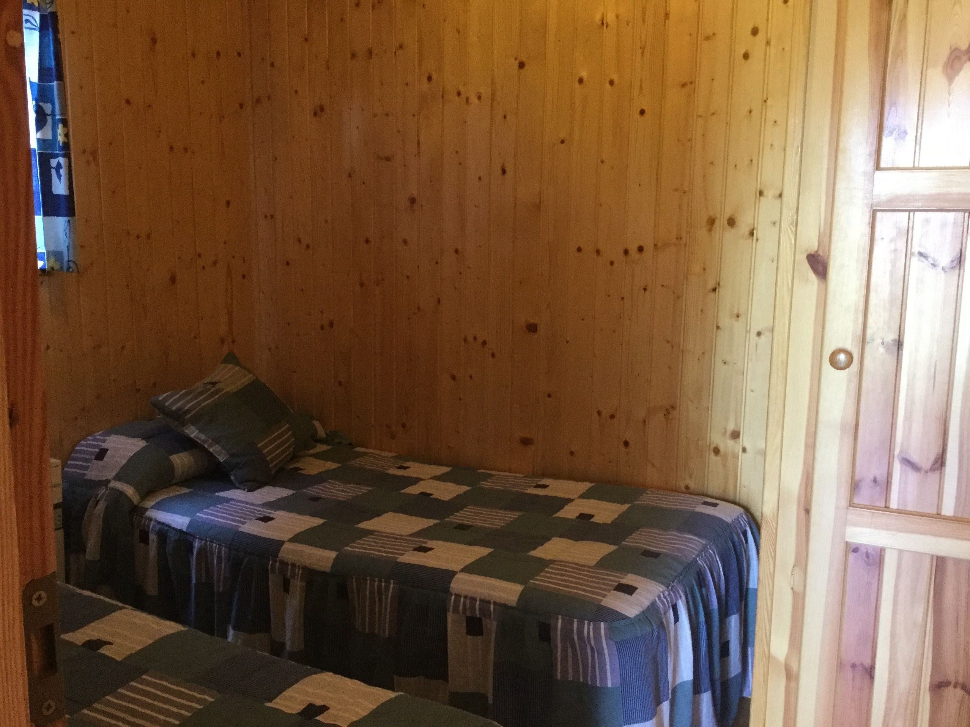 Una habitación pequeña y acogedora con paredes de madera y una cama individual con colcha a cuadros.