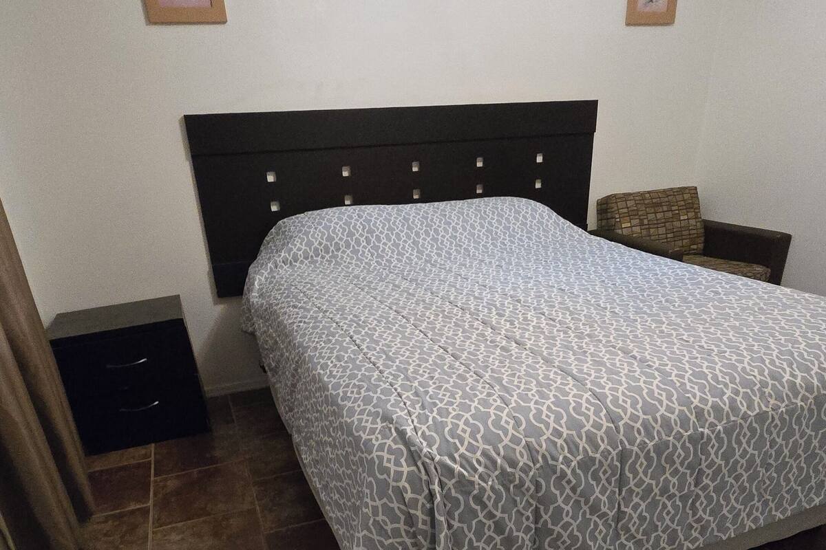 Een slaapkamer met een bed, een nachtkastje, een stoel en twee ingelijste foto’s aan de muur.