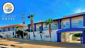 A hotel with a blue and white facade, palm trees, and a clear sky. - Hotel Villas Del Sol (Golfo de Santa Clara)