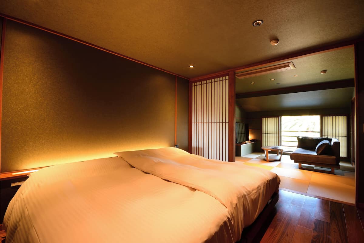 A hotel room with a large bed, a seating area with a sofa and a table, and a sliding door leading to a balcony.