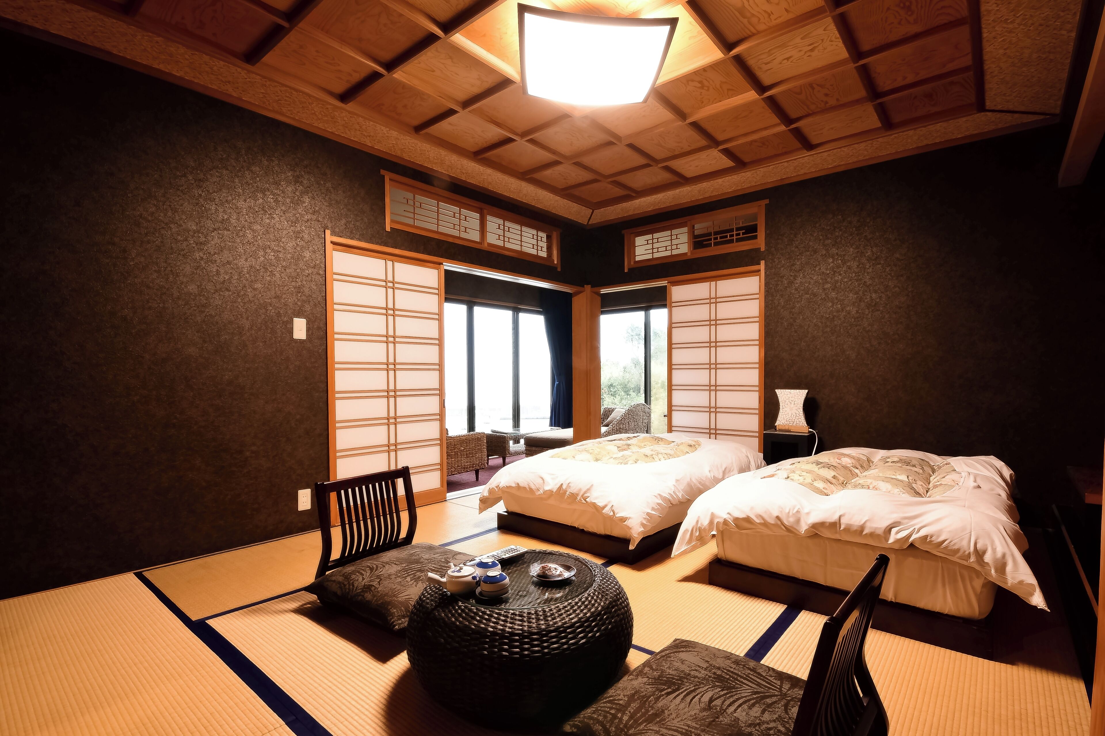 Un dormitori de planta tradicional japonesa amb paviment de tatami, dos llits, un futó, una taula baixa amb joc de te i portes corredisses.