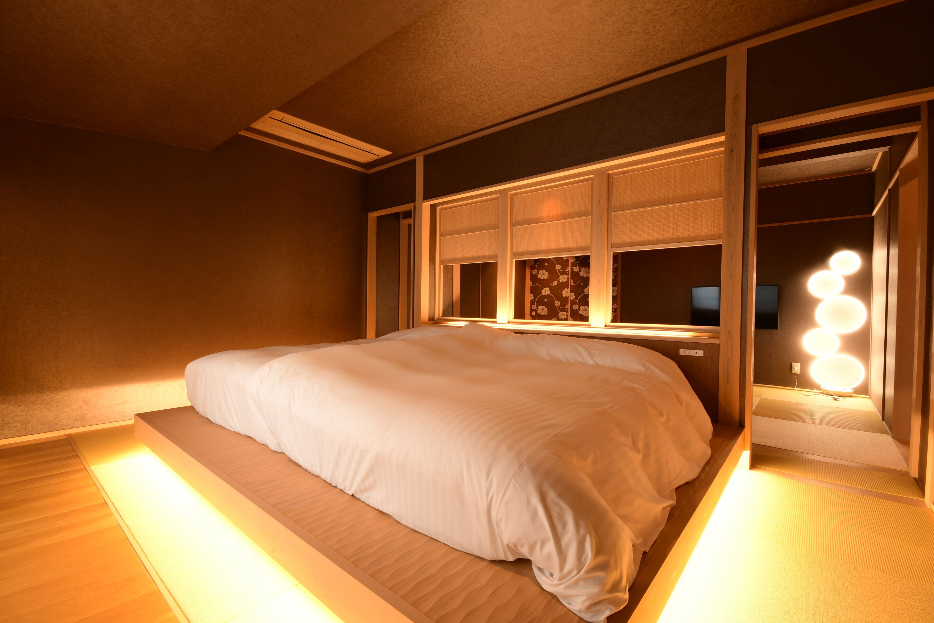 Un llit ben fet a una habitació amb una finestra gran, una tauleta de nit i un mirall amb il·luminació.