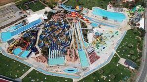 An aerial view of a water park with multiple slides and pools, surrounded by green lawns and a few buildings.
