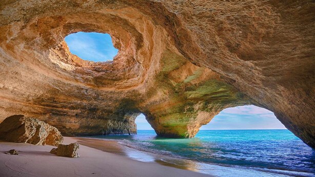 A natural rock formation with a circular opening, a sandy beach, and the sea.