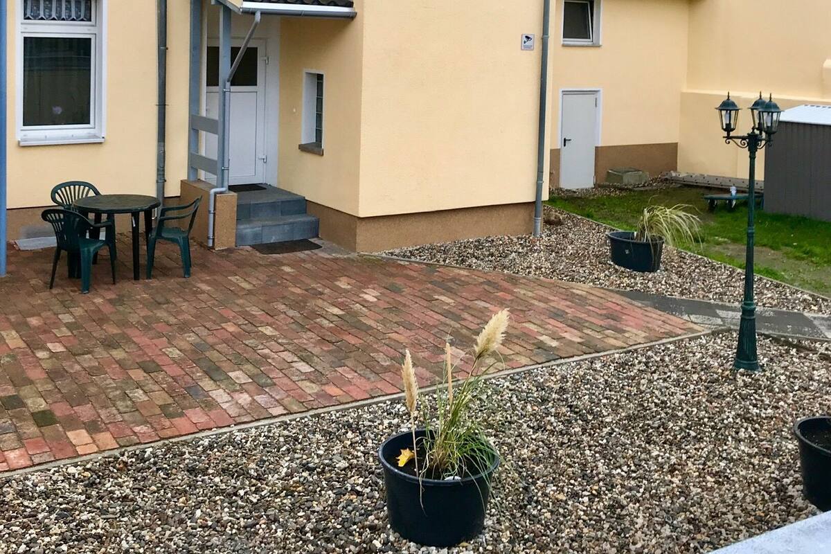 Un bâtiment jaune avec un toit en tuiles, un patio couvert avec une table et des chaises, et un chemin de gravier.