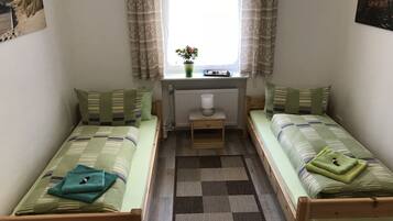A small, cozy room with two single beds, a small table, a window with curtains, and a radiator.