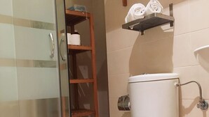 A bathroom with a toilet, a glass shower enclosure, a wooden shelf with towels, and a toilet paper holder. - IMPRESSIVE LOFT, MADRID, NEXT TO THE METROPOLITAN WANDA (Madrid)