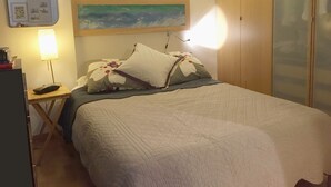 A neatly made bed with a floral pillow and a quilt, a bedside lamp, a small table with a remote control, and a wall-mounted artwork. - IMPRESSIVE LOFT, MADRID, NEXT TO THE METROPOLITAN WANDA (Madrid)