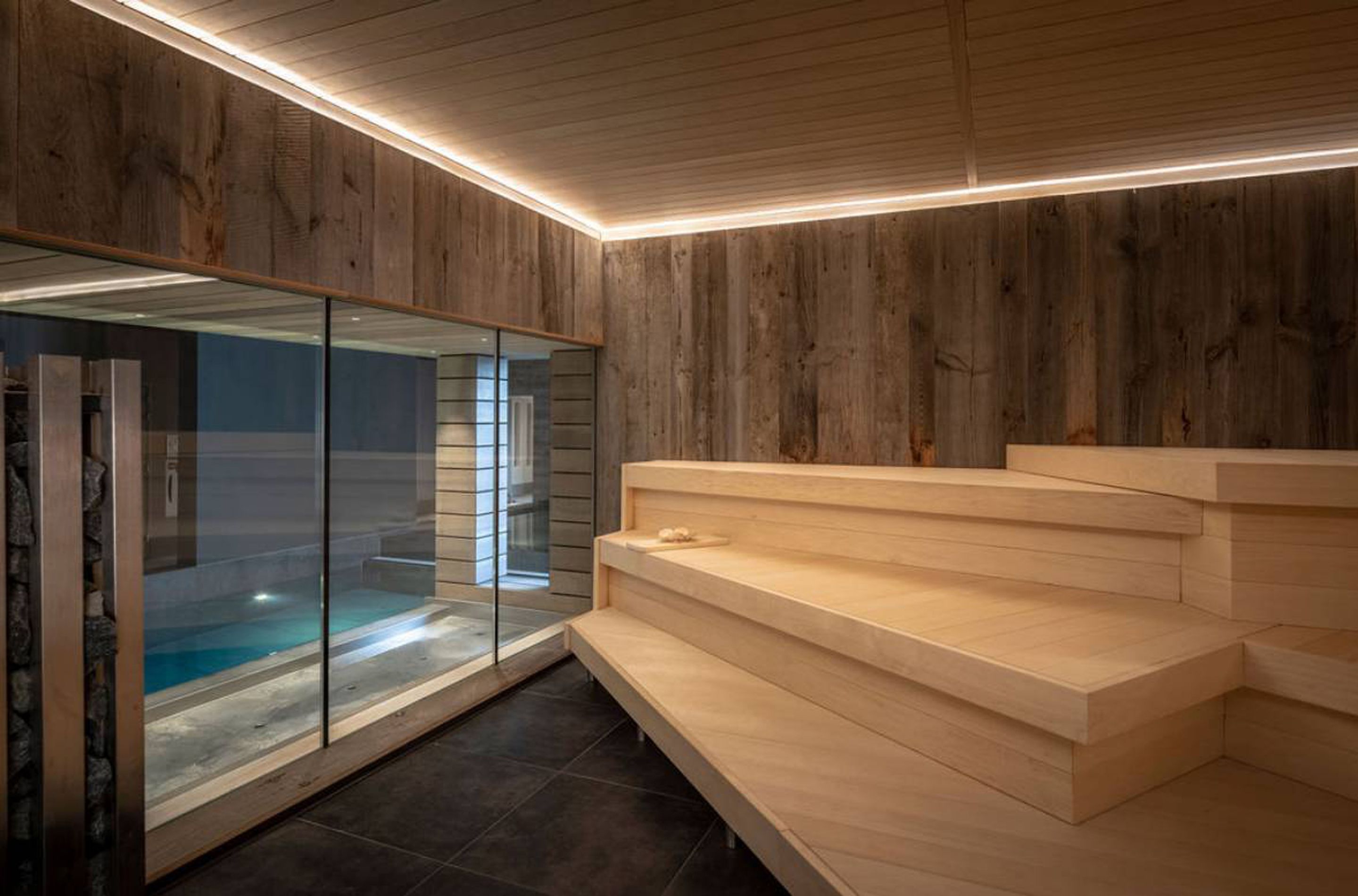 Un interior moderno con pared de madera, un recinto de vidrio con piscina y una escalera de madera.