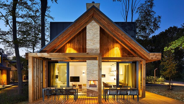 A modern cabin with a stone fireplace, wooden deck, and large glass doors leading to an interior with a dining area and seating. - Bergvliet Villa's (Oosterhout)