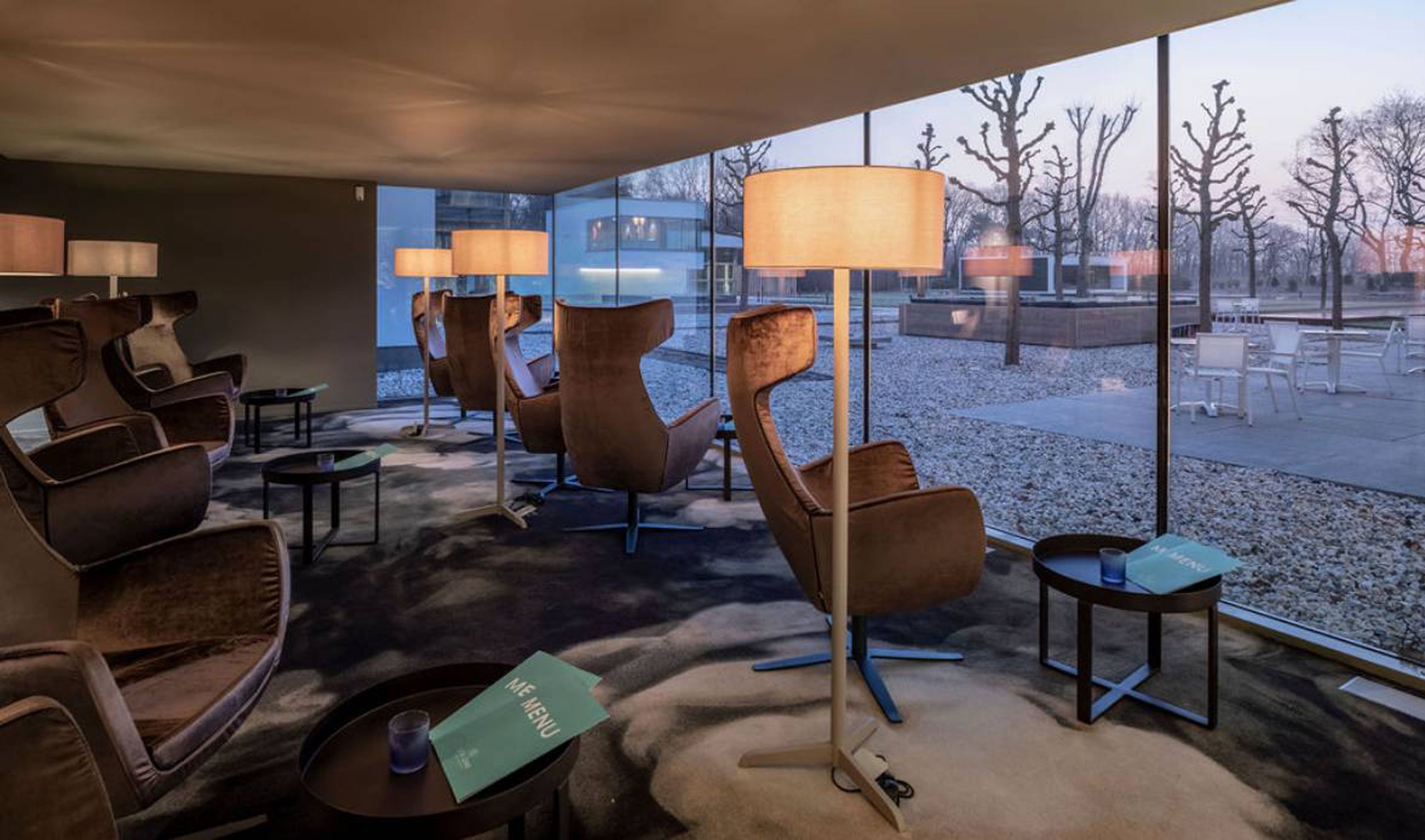 Zona relax moderna con poltrone in pelle, tavolino e lampade da terra. Un menu è visibile sul tavolo.