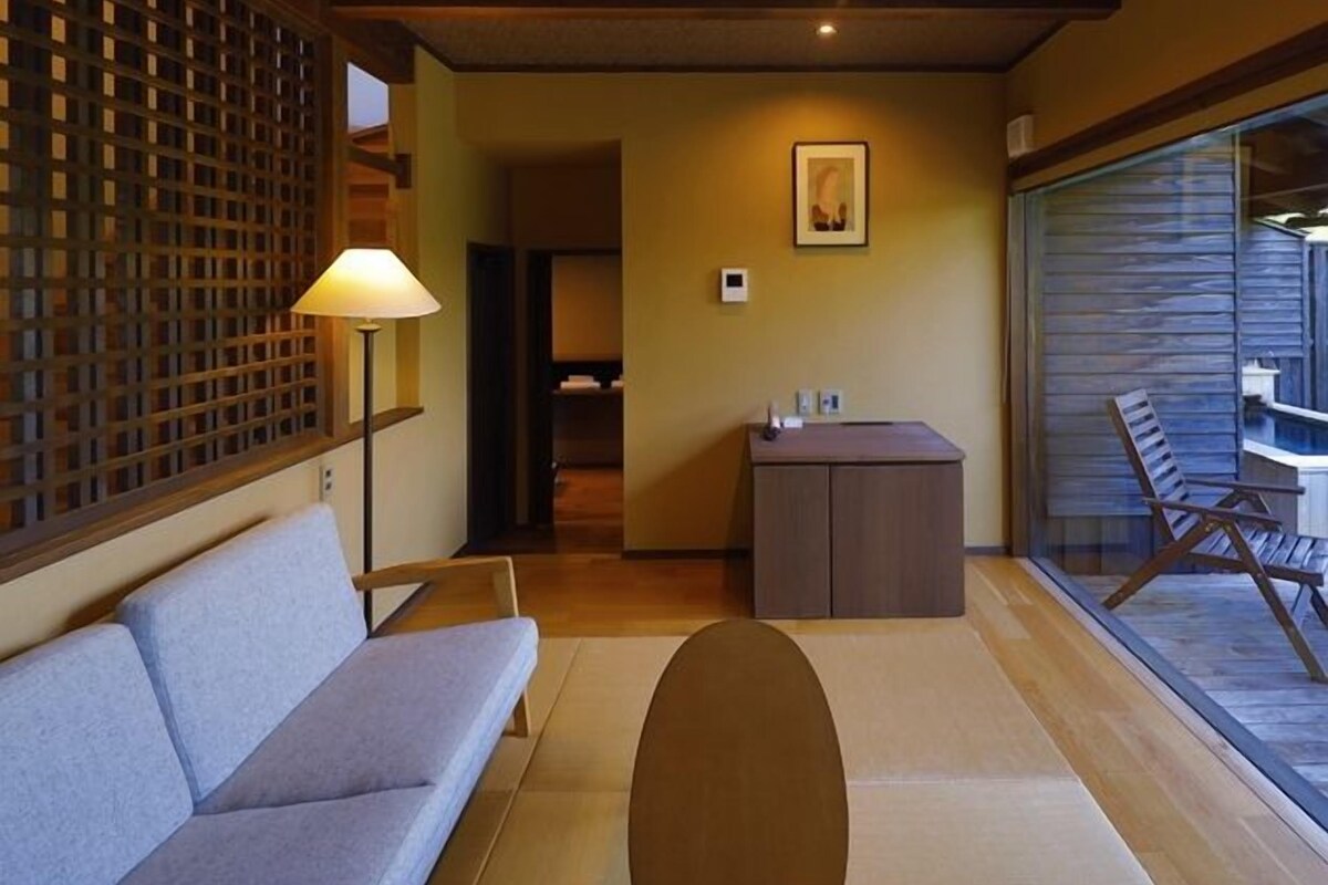 A room with a sofa, a lamp, a desk, and a view of a pool.