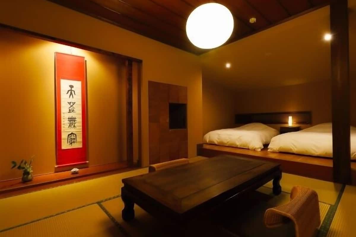 Ein traditioneller japanischer Raum mit Tatami-Boden, einem niedrigen Holztisch, einem Bett mit weißer Bettwäsche und einem roten Schild mit japanischen Schriftzeichen.