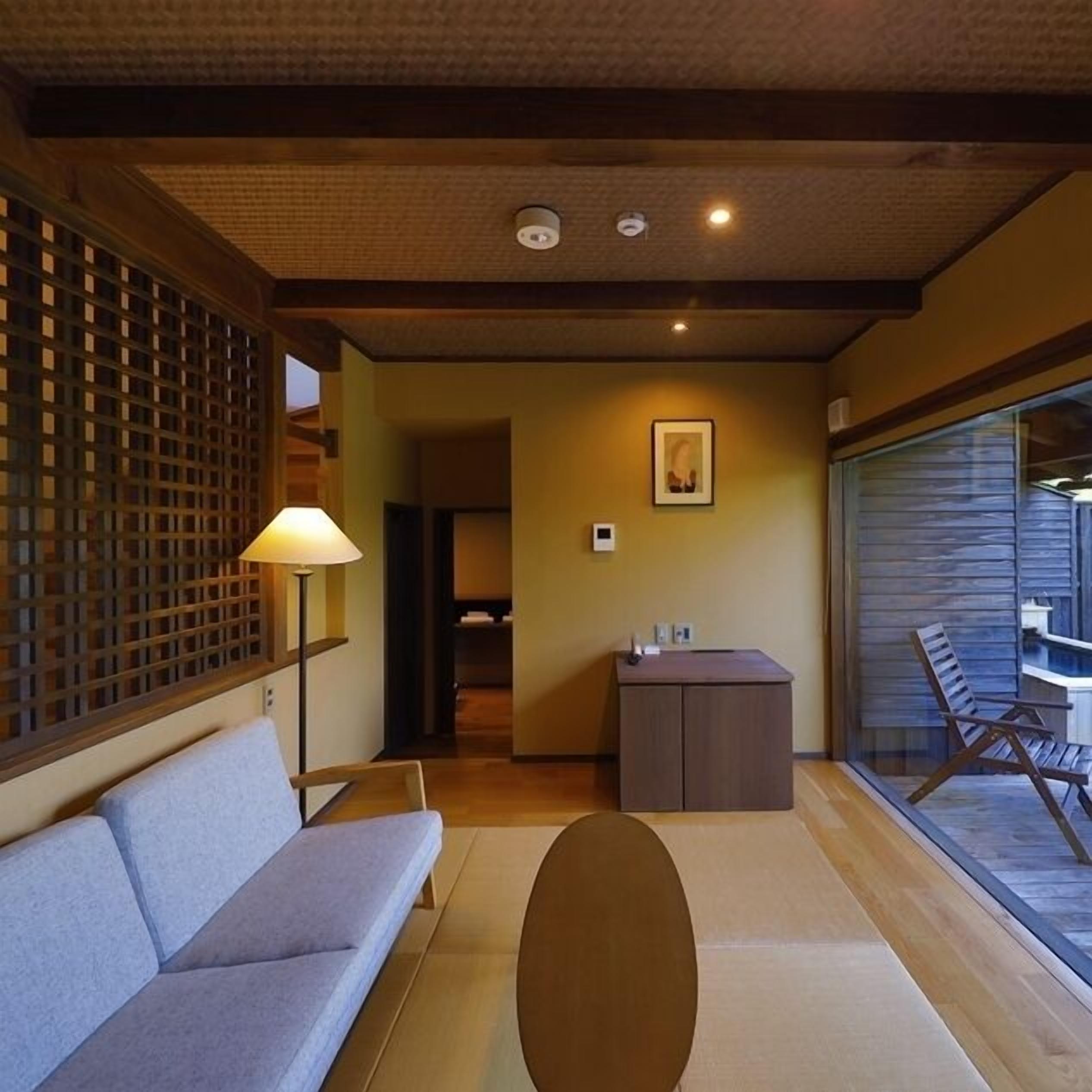 A room with a sofa, a lamp, a desk, and a view of a pool.