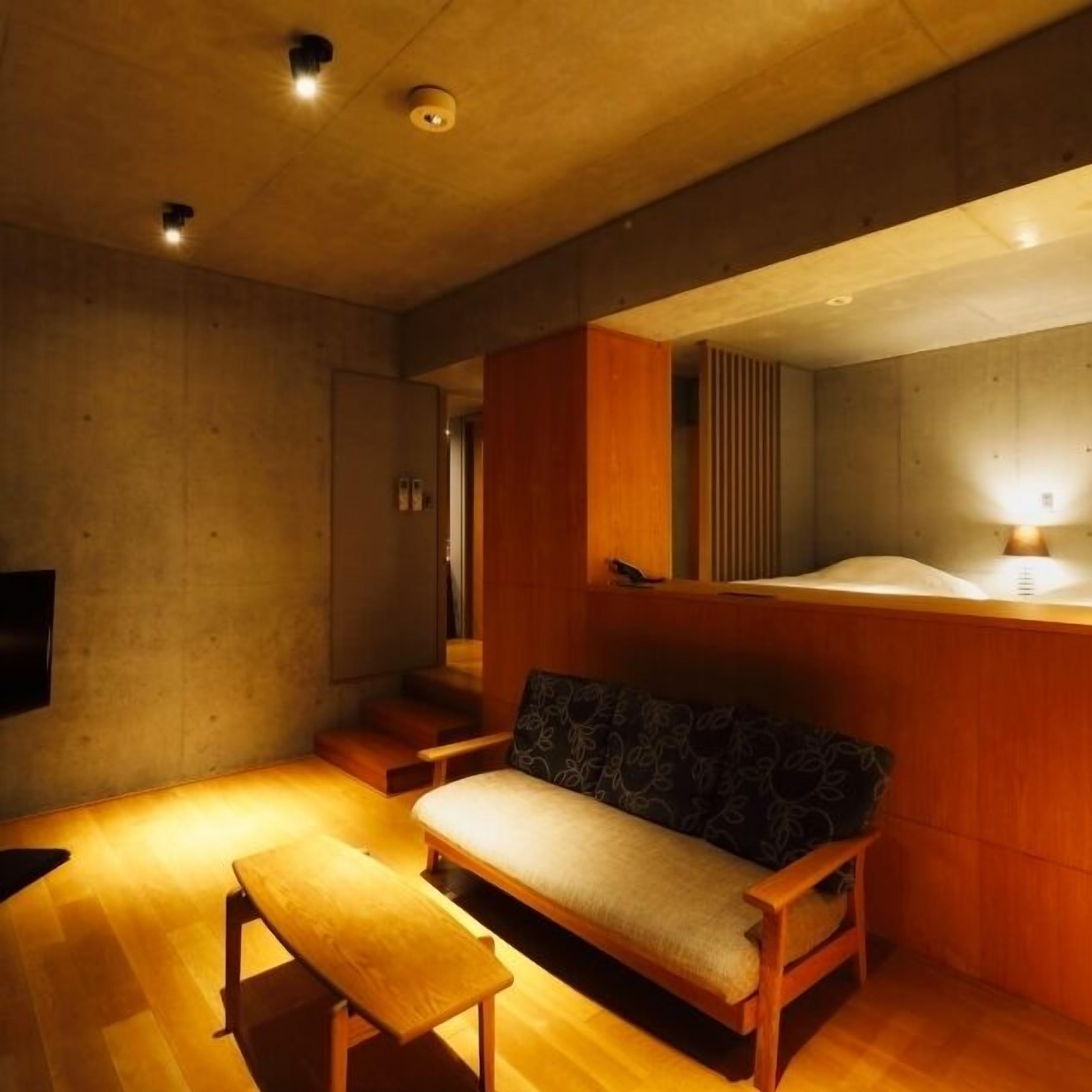 Una habitación con un banco de madera, un sofá, un televisor y una lámpara fijada a la pared.
