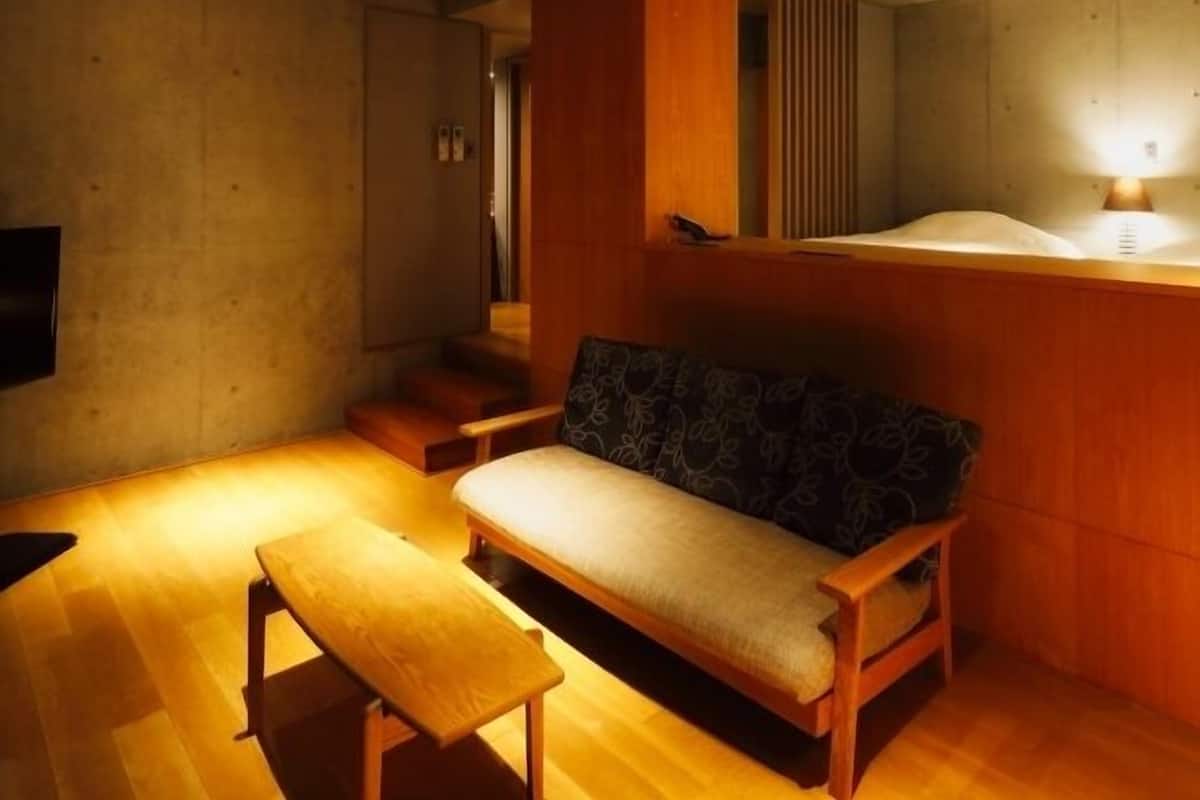 Ein Zimmer mit einer Holzbank, einem Sofa, einem Fernseher und einer Wandleuchte.