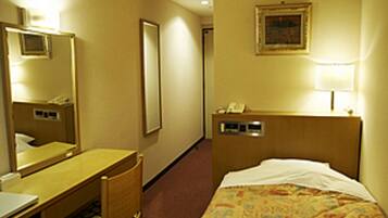 A hotel room with a bed, a desk, a chair, a mirror, a bedside table, and a lamp.