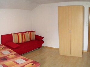Een kamer met een rode bank, gestreepte kussens en een houten garderobe.