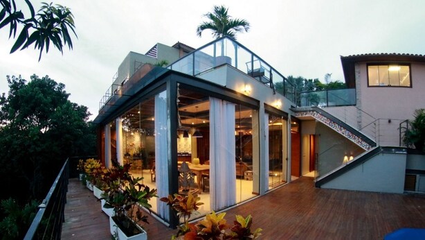 A modern house with a glass-enclosed patio area, a wooden deck, and a staircase leading to a second floor. - Villa Puerto Nuevo (Búzios)