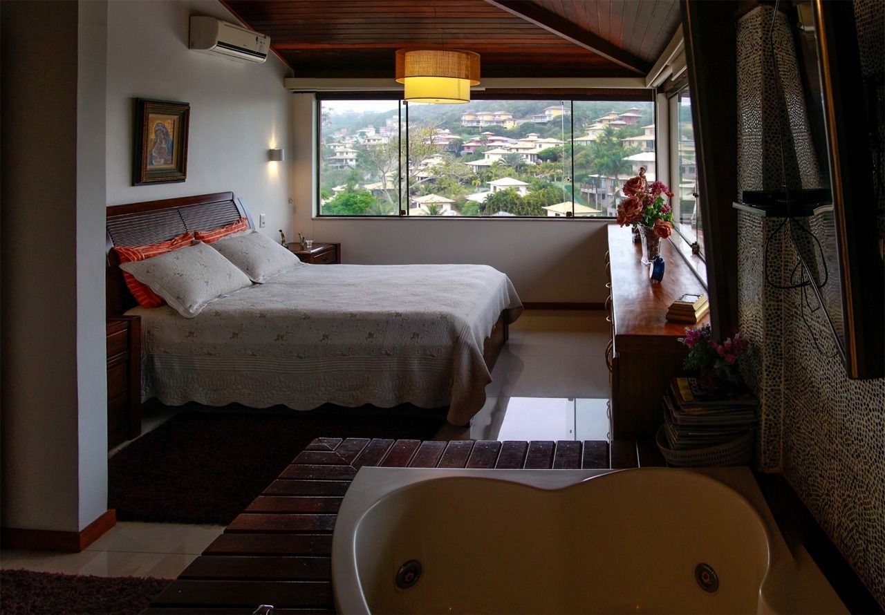 A bedroom with a bed, a nightstand, a bedside table with a vase of flowers, a window with a view of a hillside, and a bathtub.