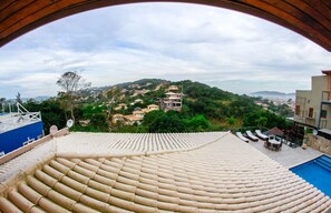 A rooftop terrace with a pool and lounge chairs, overlooking a hillside with buildings. - Villa Puerto Nuevo (Búzios)