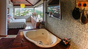A bedroom with a large window, a wooden ceiling, a bed, a vanity with a mirror, and a bathtub. - Villa Puerto Nuevo (Búzios)