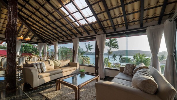 A spacious living area with a large window offering a view of the sea and palm trees. There are two sofas and a coffee table. - Villa al mare (Búzios)