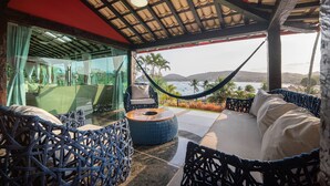 A covered outdoor seating area with wicker furniture, a hammock, and a view of the ocean. - Villa al mare (Búzios)