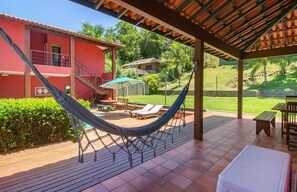 A covered outdoor area with a hammock, lounge chairs, and a patio table. - Villa La Plage (Búzios)