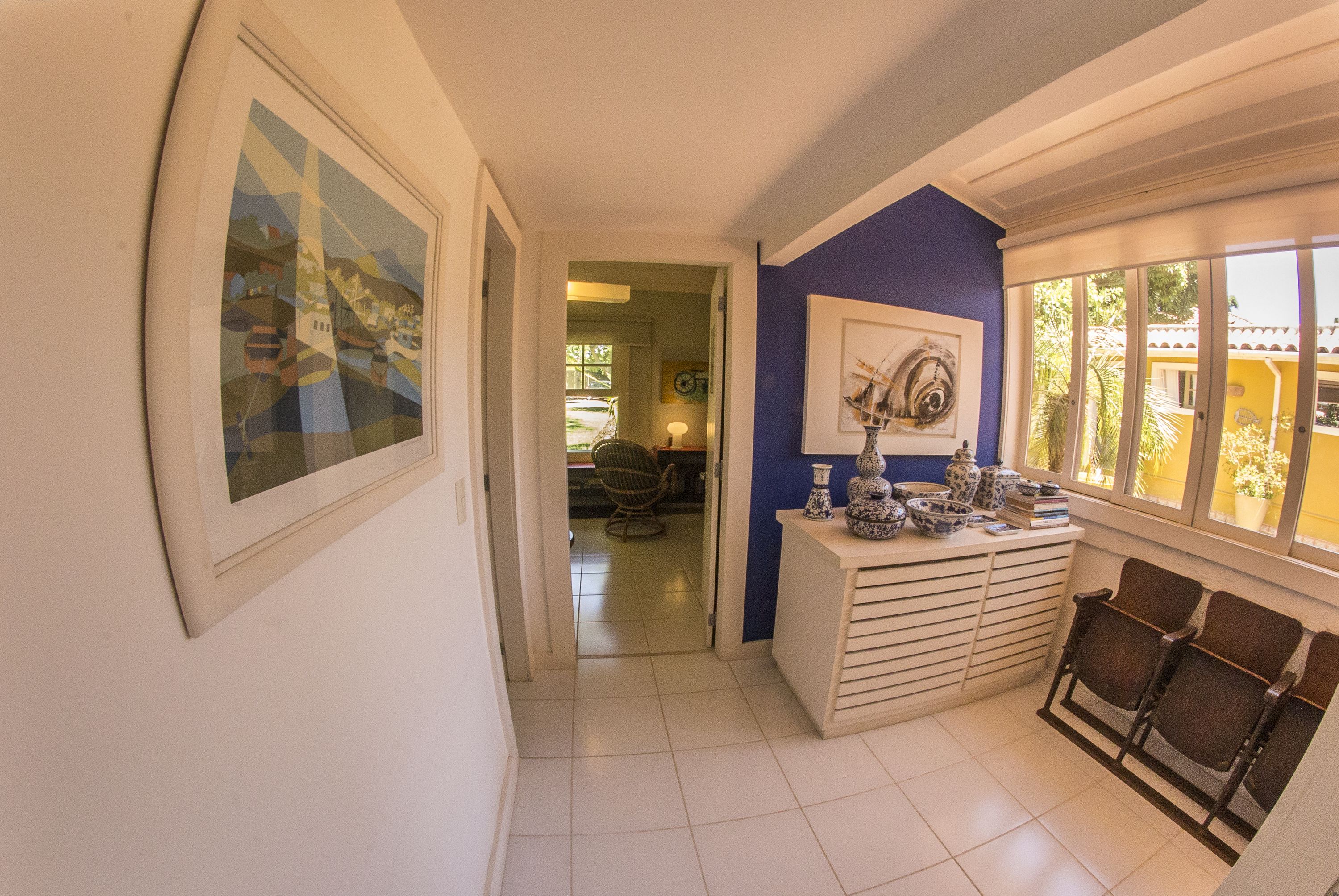 A hallway with a framed picture, a blue wall, a window with a view, and a small table with decorative items.
