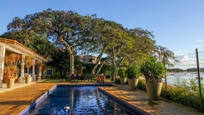 A swimming pool with a wooden deck, surrounded by potted plants and trees. -  Villa Manguinhos (Búzios)